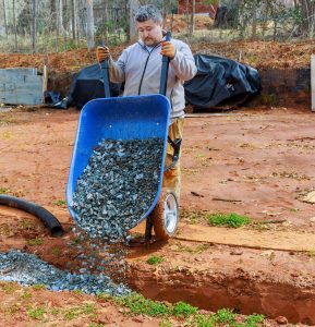 man dumping stones into french drain
